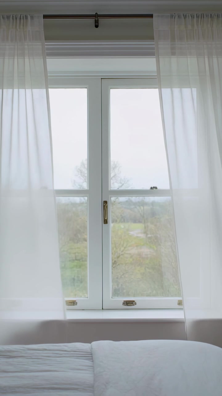 Vertical video: Swaying sheer curtains on white window in bedroom revealing field by gentle breeze