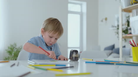 el niño dibuja con un lápiz de color sentado en la mesa en la sala de estar