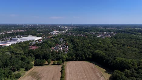 Agricultural farm fields, green forest trees, small suburb neighborhood and industrial warehouse in summer. Small American town cityscape with blue sky and sunlight. Aerial forward wide shot
