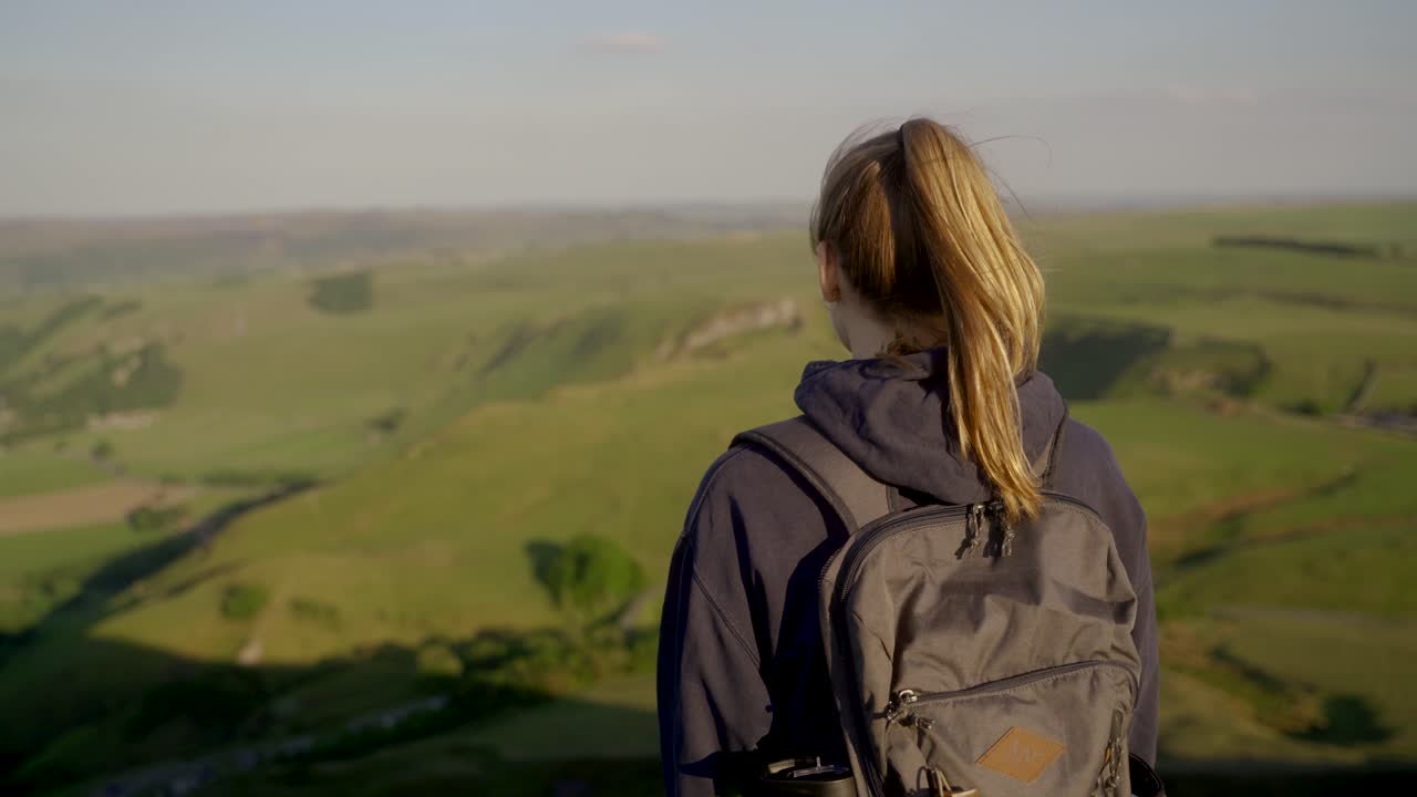 tiro giratorio de mano de una joven rubia admirando la vista desde la cima de mam tor, castleton, distrito de los picos, inglaterra al atardecer