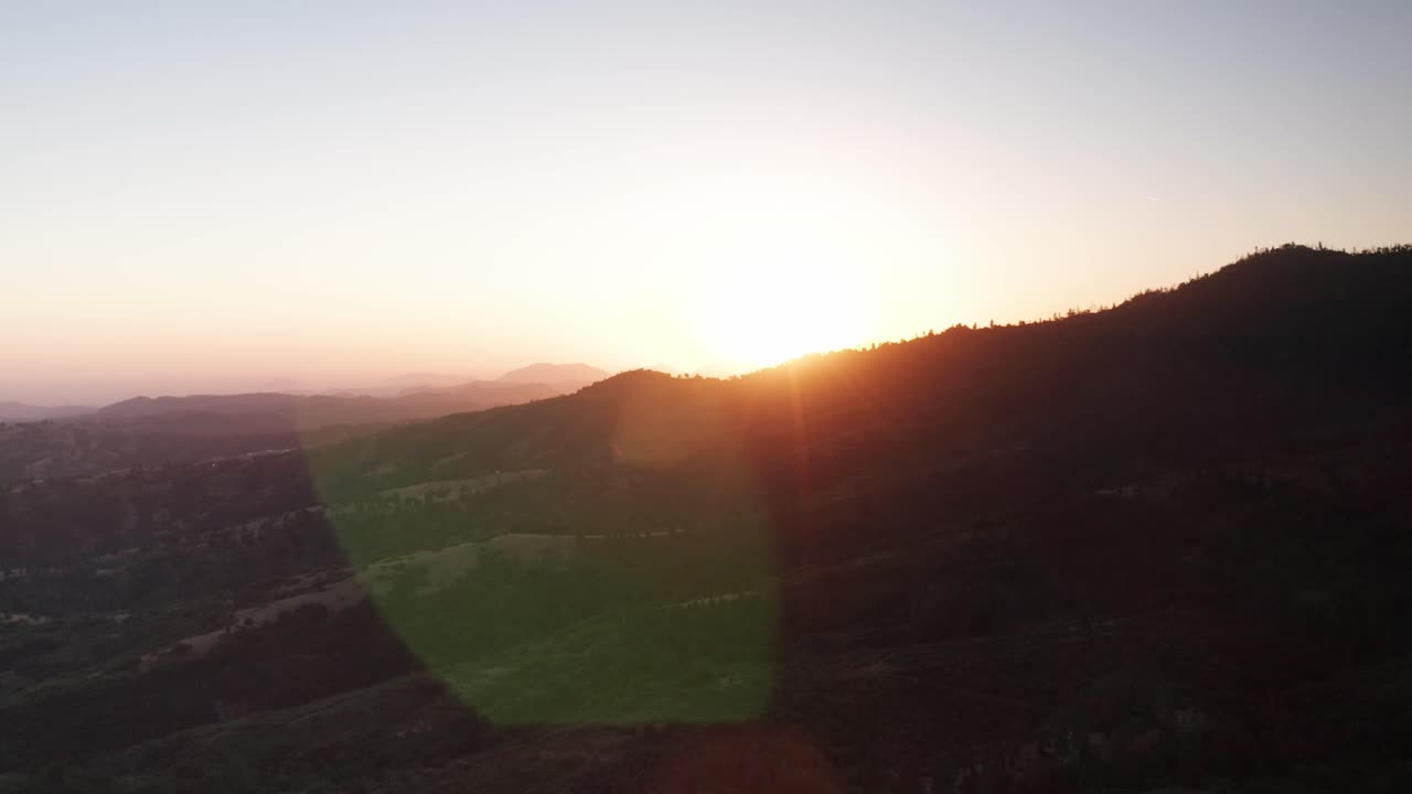 석양에 렌즈 플레어가 있는 산등성이를 엿보는 태양의 왼쪽에서 오른쪽으로 패닝 공중 촬영