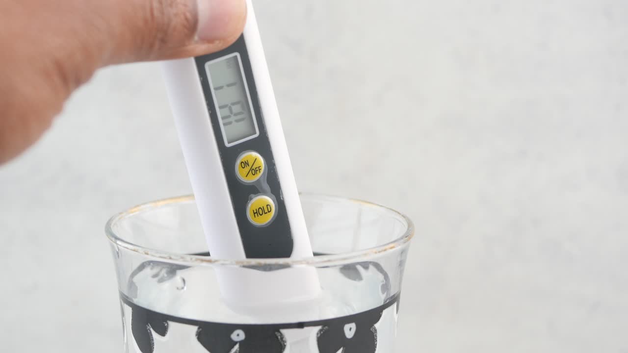Hand holding a digital pH meter in a glass of water