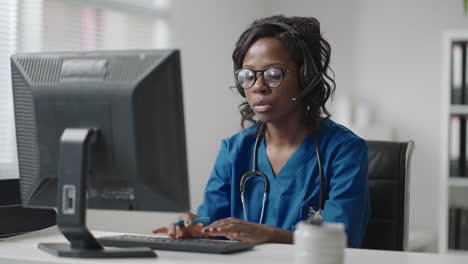 Black-Woman-doctor-wear-white-coat-glasses-and-headset-talking-to-client-use-videocall.-Due-coronavirus-pandemic-outbreak-therapist-working-remotely-provide-help-to-clinic-patients-by-video-call