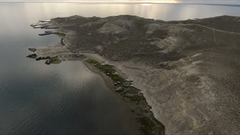 flying above wild barren landscape of patagonia with beautiful seashore at sunset - aerial tilt-up shot