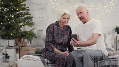 happy senior couple sitting on bed making a video call on christmas morning