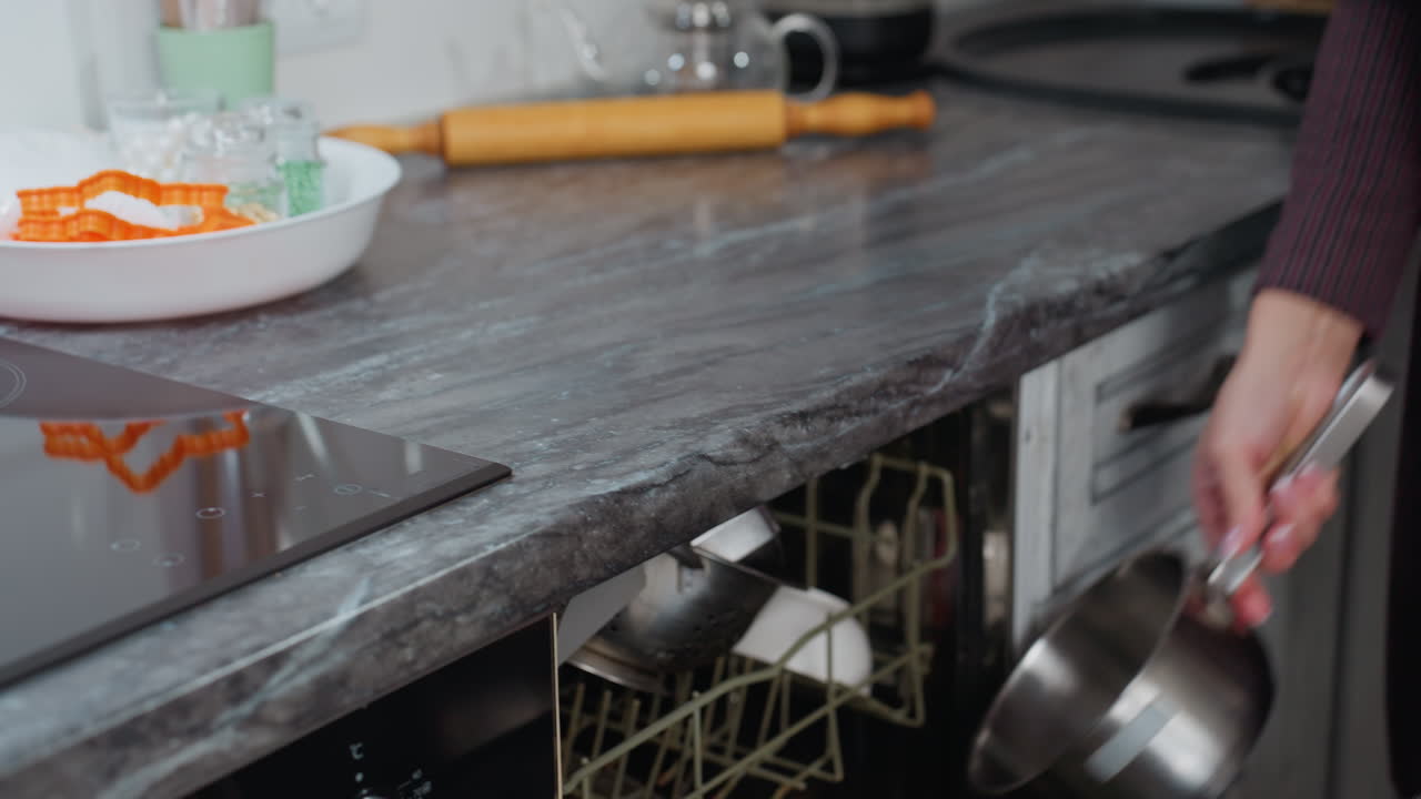 женщина рядом с индукционной печью готовится печь в современном кухонном интерьере с пекарными инструментами, мраморной столовой и кухонной посудой на размытом фоне