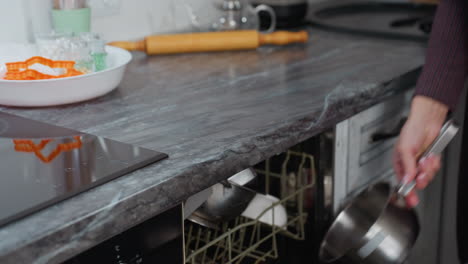 mujer mano cerca de la estufa de inducción preparándose para hornear en el interior de la cocina moderna con herramientas de horneado, encimera de mármol y utensilios de cocina en un fondo borroso