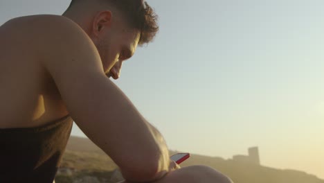 hombre sentado en la orilla del mar y navegando por teléfono inteligente