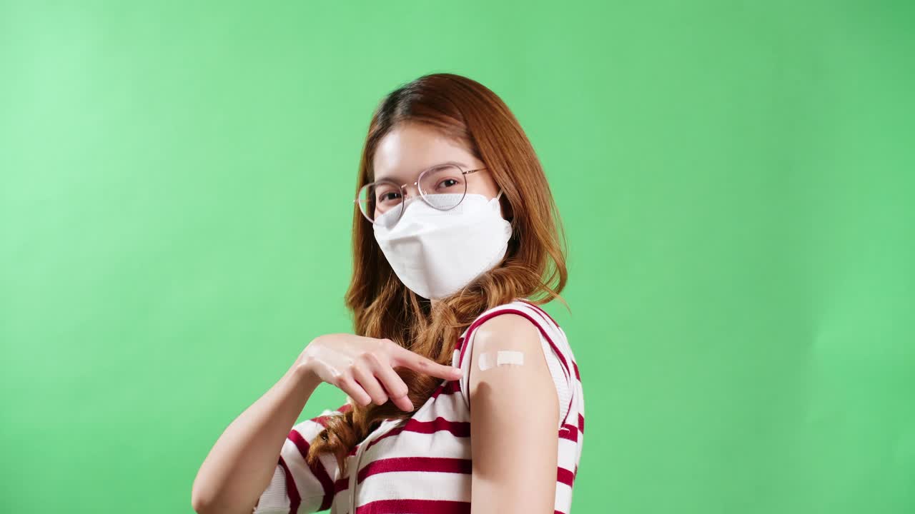 joven asiática señalando su brazo después de ser vacunada contra covid-19 en estudio con fondo de clave cromática