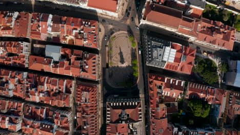 Descending-overhead-top-down-aerial-view-of-small-public-square-with-a-monument-surrounded-by-red-rooftops-of-traditional-Portuguese-houses-in-Lisbon-city-center