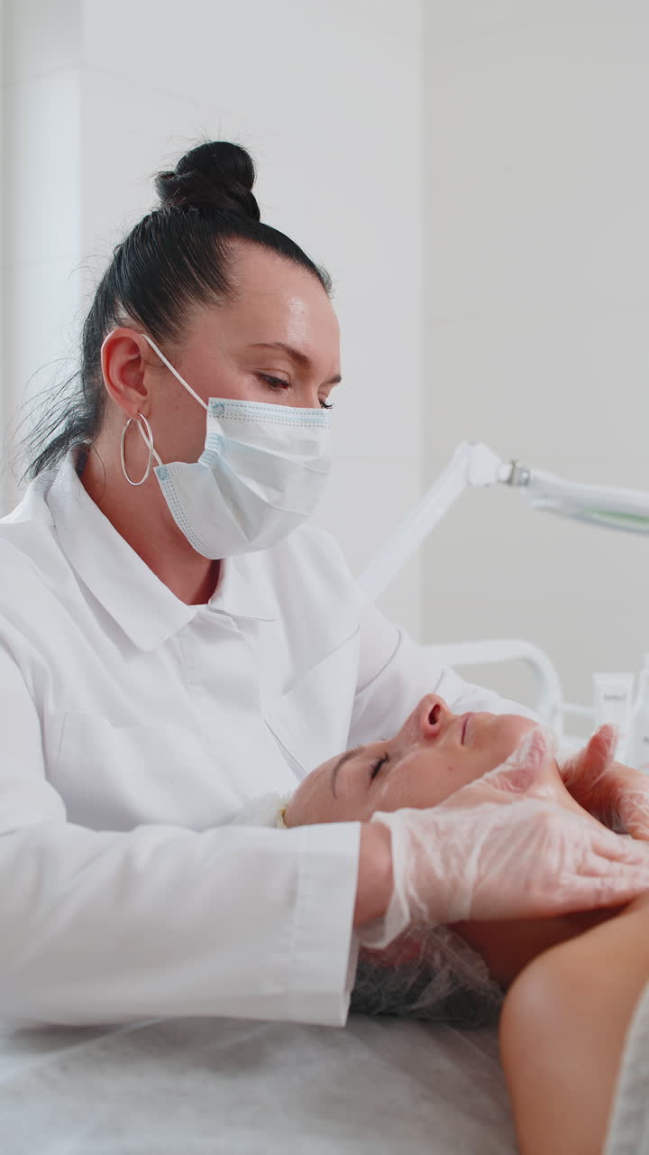 Cosmetologist applying moisturizing medical chemical peeling cream mask on young adult woman face