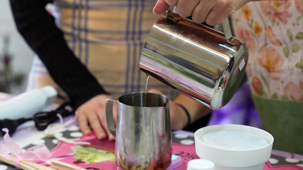Artisan carefully pouring melted wax into a metal jug over a scale during a candle making workshop