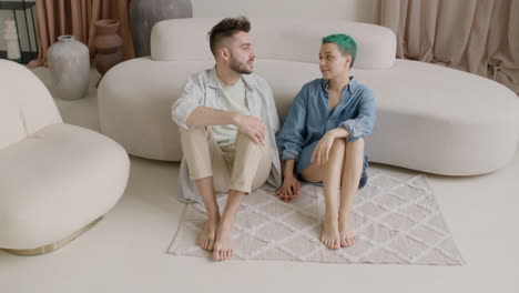 barefoot couple holding hands and talking together while sitting on a carpet at home