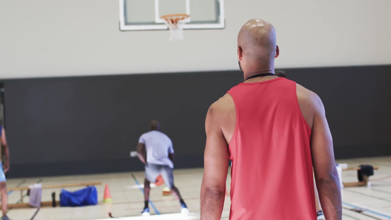 entrenador de baloncesto masculino diverso viendo el juego de entrenamiento del equipo en la cancha cubierta, en cámara lenta