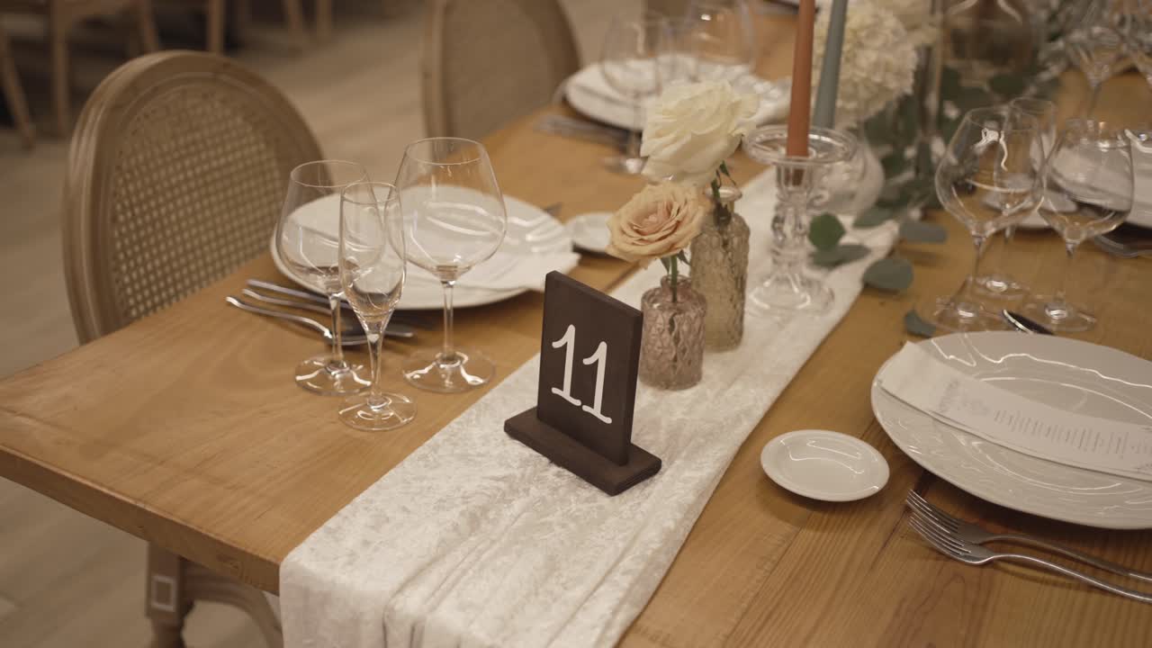 Decorated wedding reception table with plates glassware candles flowers and table number sign on wooden table