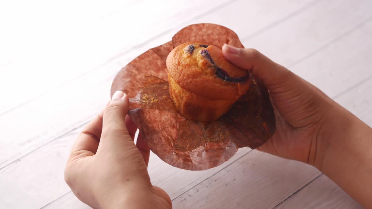 Hands holding a blueberry muffin in brown paper