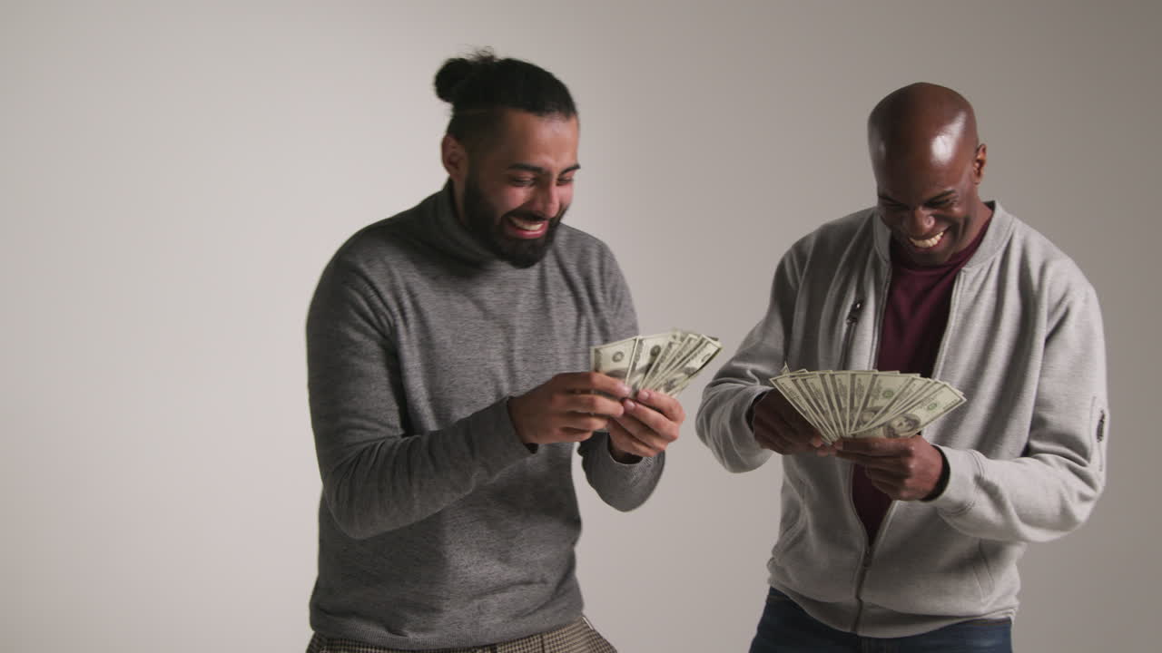 Studio Shot Of Two Excited Male Friends Celebrating Winning Cash Prize Throwing Handful Of 100 Dollar Bills In The Air