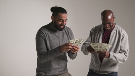 fotografía de estudio de dos amigos masculinos emocionados celebrando el premio en efectivo lanzando un puñado de billetes de 100 dólares en el aire