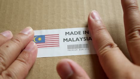 hands applying made in malaysia flag label on a shipping box with product premium quality barcode