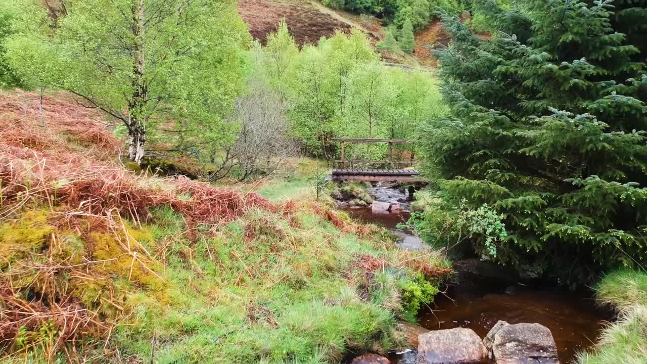 filmische drohnen-zoomaufnahme des schottischen highland creek mit kleiner brücke im hintergrund