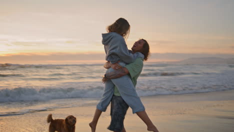 una pareja juega en la playa al atardecer con un perro.