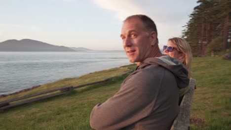 beautiful adult family kiss while watching sunset on coastline bench, motion view