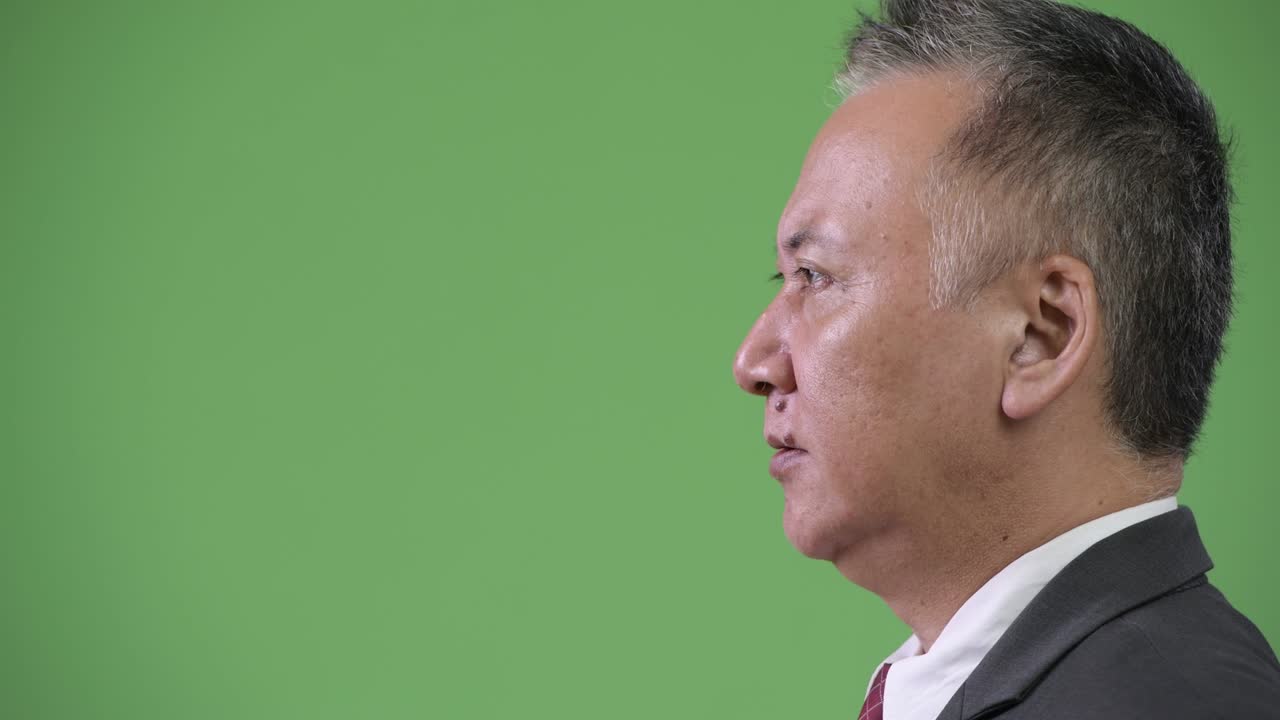 Yeşil arka plan önünde bağıran olgun sinirli Japon iş adamının profil görünümü.