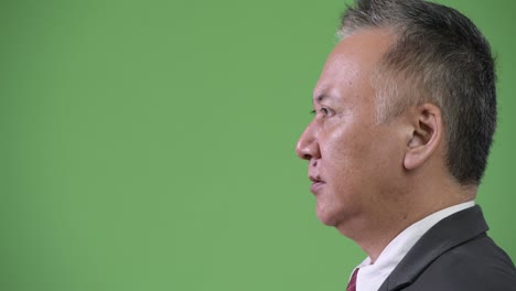 profile view of mature angry japanese businessman shouting against green background