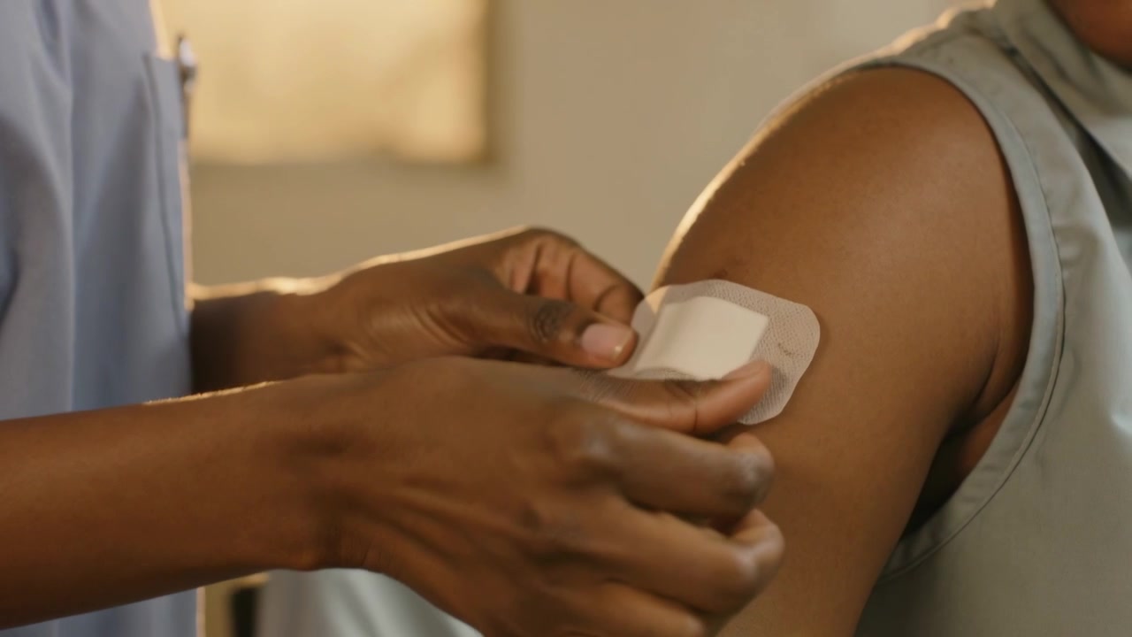 Infermiera in camice blu che applica una medicazione sul braccio del paziente dopo un'iniezione, in clinica, con spazio per il testo.
