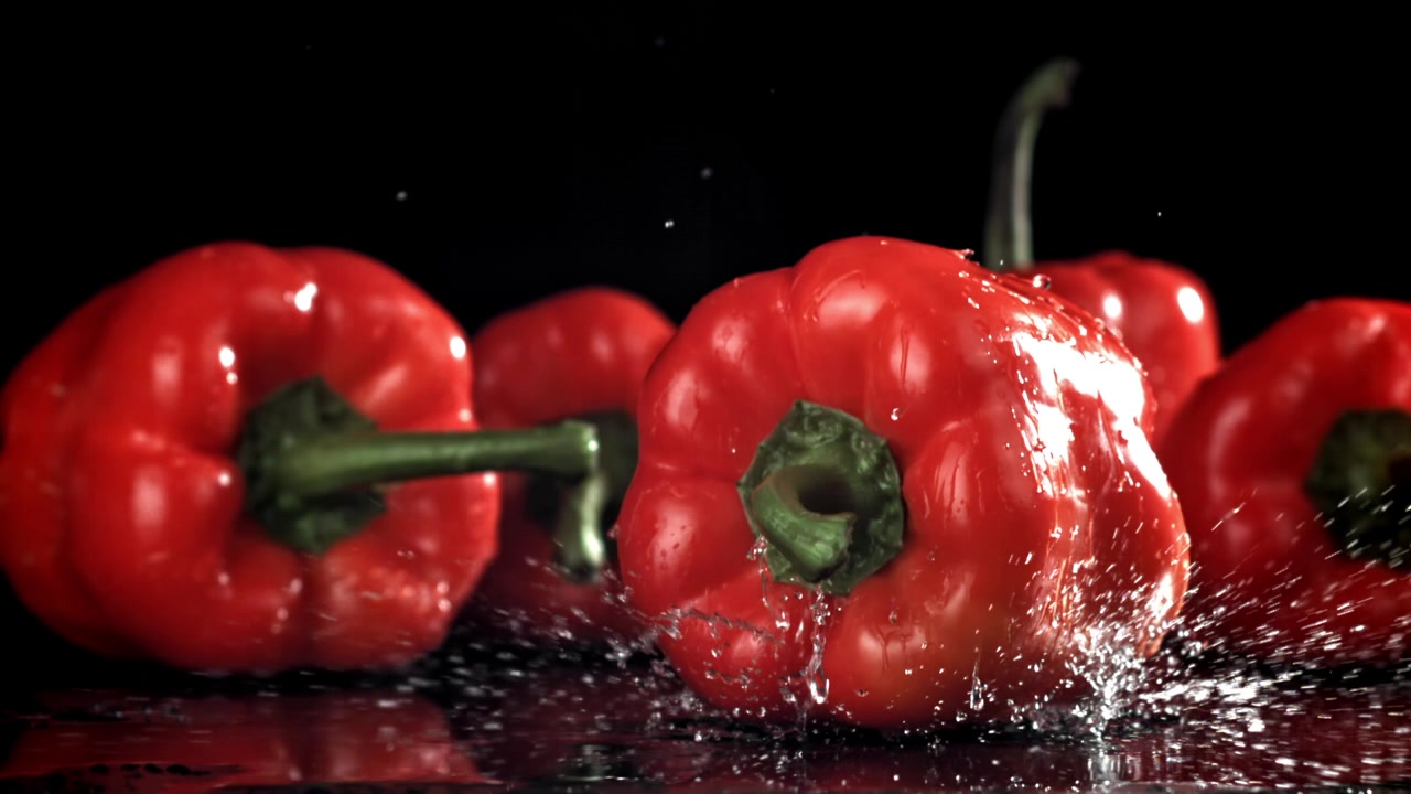 Červená paprika padající zpomaleně s cákanci vody.