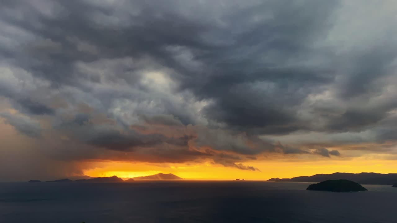 Lapso de tiempo aéreo de enormes nubes de tormenta oscuras formándose sobre el océano durante un atardecer dorado. Una dramática exhibición meteorológica que muestra patrones climáticos pre-tifón sobre el mar y las islas.