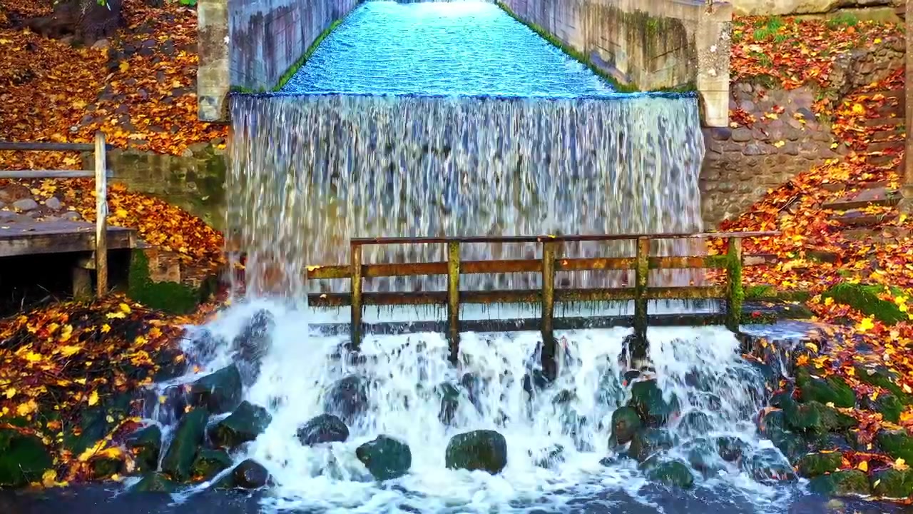 Bellissima cascata che scende a cascata da una struttura in cemento sopra le rocce durante una tranquilla giornata autunnale