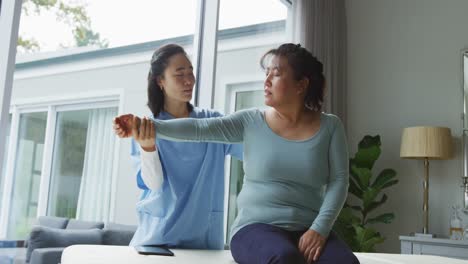 Fisioterapeuta-Asiática-Que-Trata-A-Una-Paciente-En-Cirugía,-Moviendo-Su-Brazo