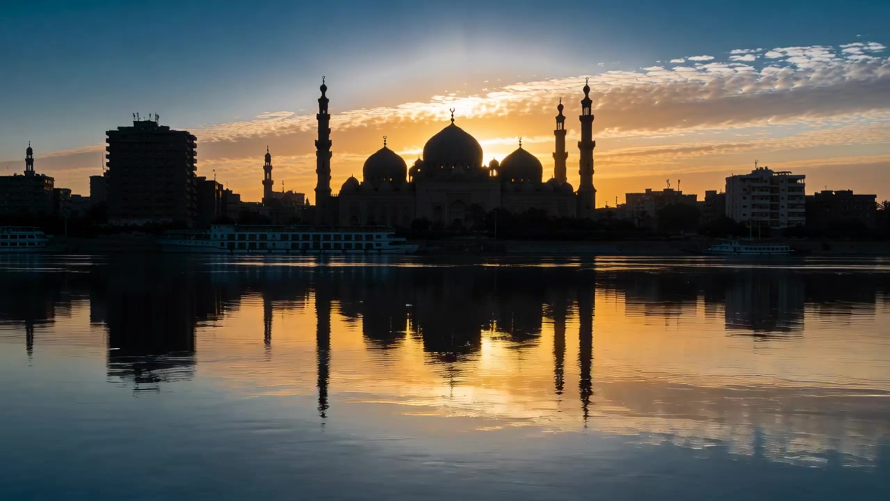 Moschea illuminata con cupole, minareti, sole basso che crea un bagliore sul fiume, riflettendo lo skyline