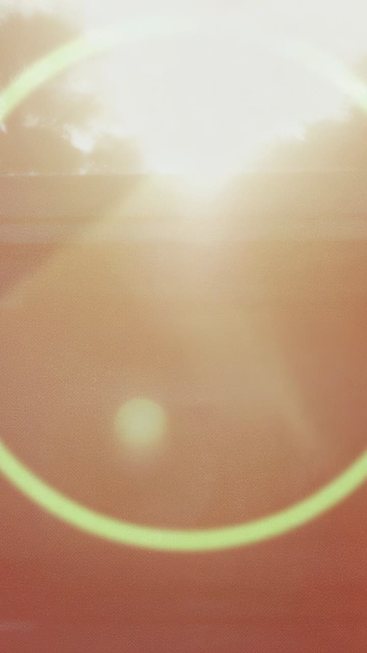 Vertical video: Rising sun creating expanding green flare ring along rooftop and tree silhouettes