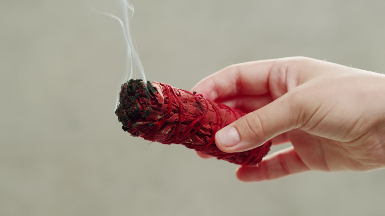 Person holding Palo Santo wood stick in hand, aromatic Palo Santo burning on black background, smoke spreading around, slow motion video clip, high quality 4k close up footage. High quality 4k footage