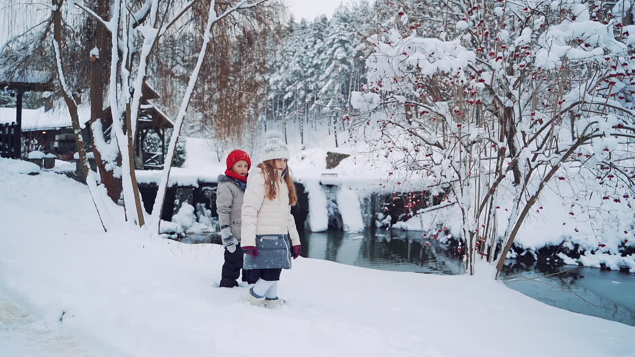 Beautiful view of natural winter background and children standing near the river. Little kids are looking at river in winter in the forest.