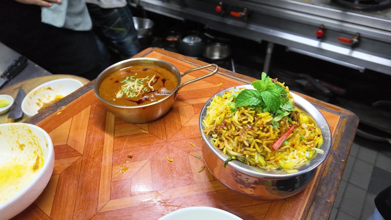 Højt vinkelbillede af aromatisk biryani-ris og krydret karry på et forberedelsesbord af træ.