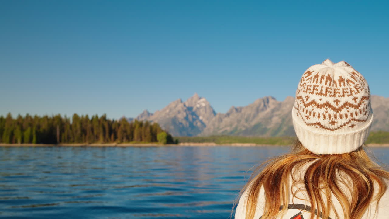 Person in knit hat overlooking a serene lake with mountains