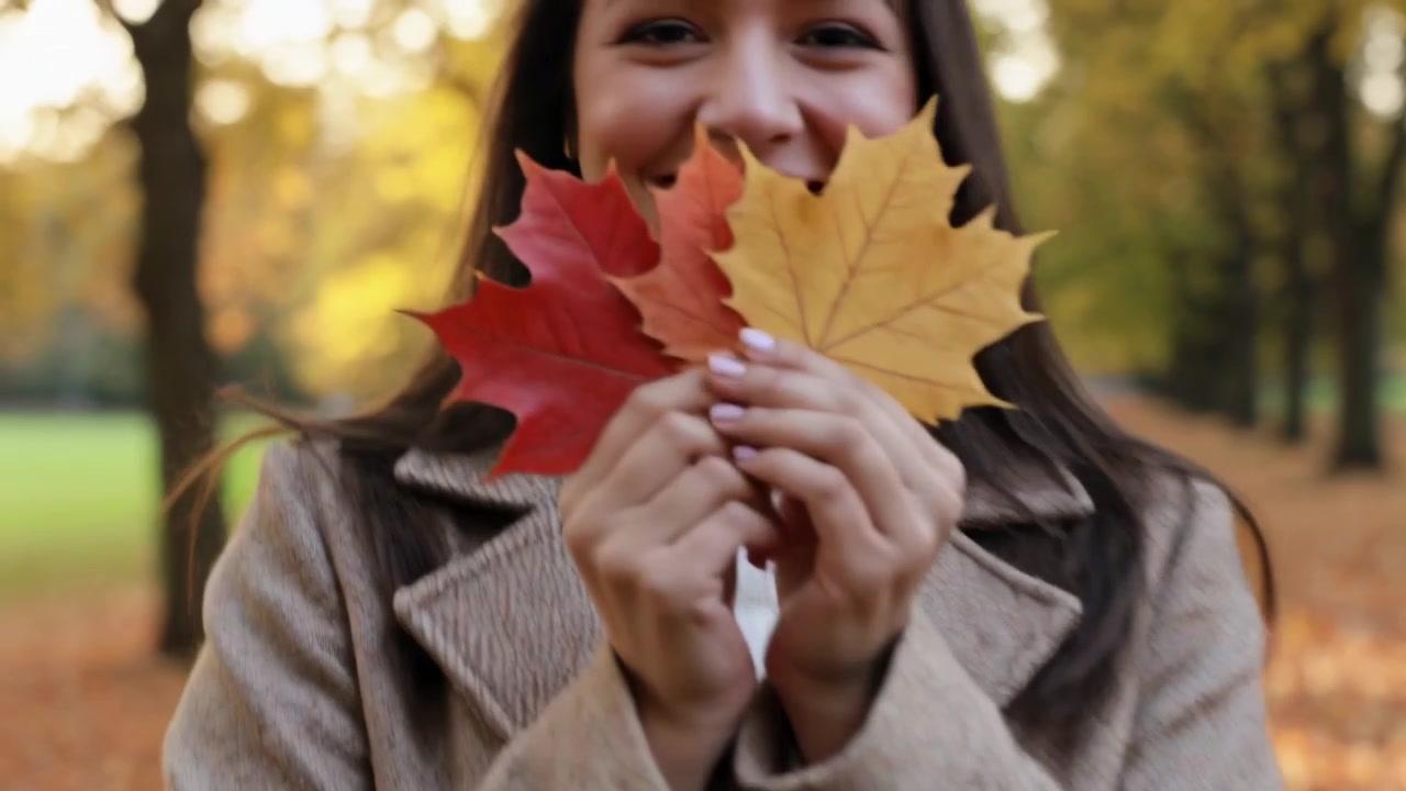Donna che cammina con un cappotto beige e stivali neri, ammirando le foglie d'acero su un sentiero del parco, mentre la telecamera si alza.