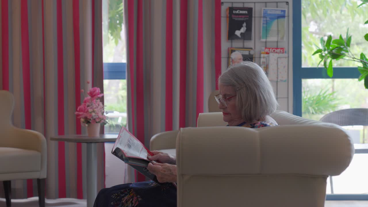 노인 여성 은 편안 한 소파 에 앉아 잡지 를 읽는 일 에 몰두 하고 있다