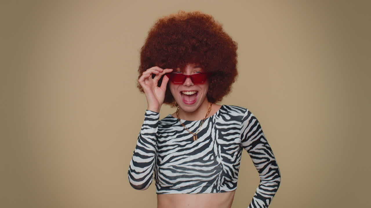 joven feliz con peluca marrón exuberante escuchando música y bailando discoteca divirtiéndose