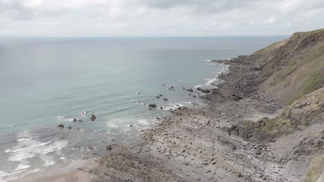 Aerial-orbital-view-of-waves-gently-lapping-against-the-rocky-North-Atlantic-coastline-of-Cornwall,-United-Kingdom