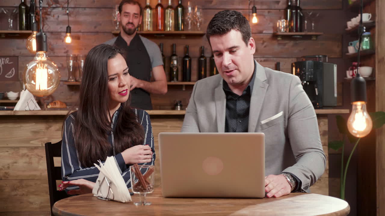 People at a bar with a waiter and a laptop on the table