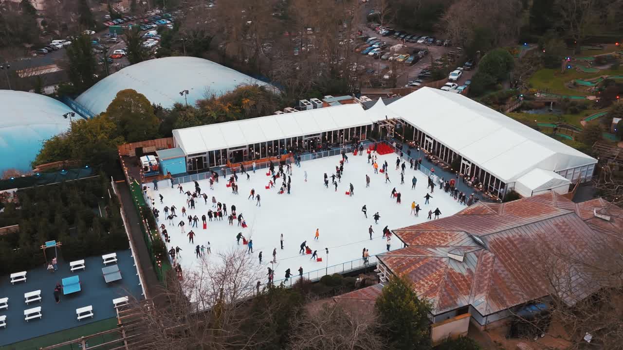 Ripresa aerea diurna con drone che orbita attorno a persone che pattinano sul ghiaccio all'aperto al Royal Victoria Park, Bath, Regno Unito