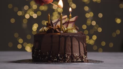 foto de estudio de pastel de celebración de cumpleaños de chocolate decorado con velas encendidas contra la iluminación de fondo del bokeh