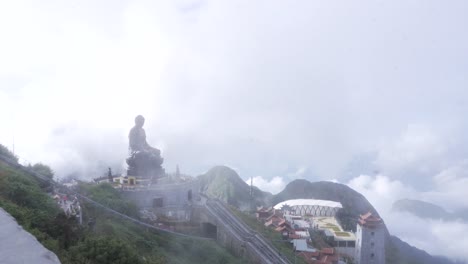 serene view of a grand amitabha buddha statue atop mist-clouded mountains with staircase leading to buddhist temple complex, stone tower and cable car station at mount fansipan, the summit of vietnam.