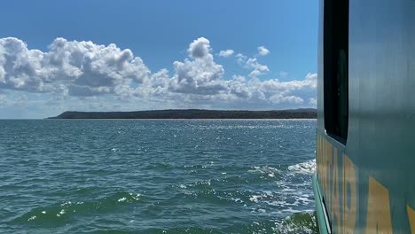 glittering ocean and blue skies with fluffy white clouds from a boat steaming towards an idyllic and tranquil pacific island off the coast of australia