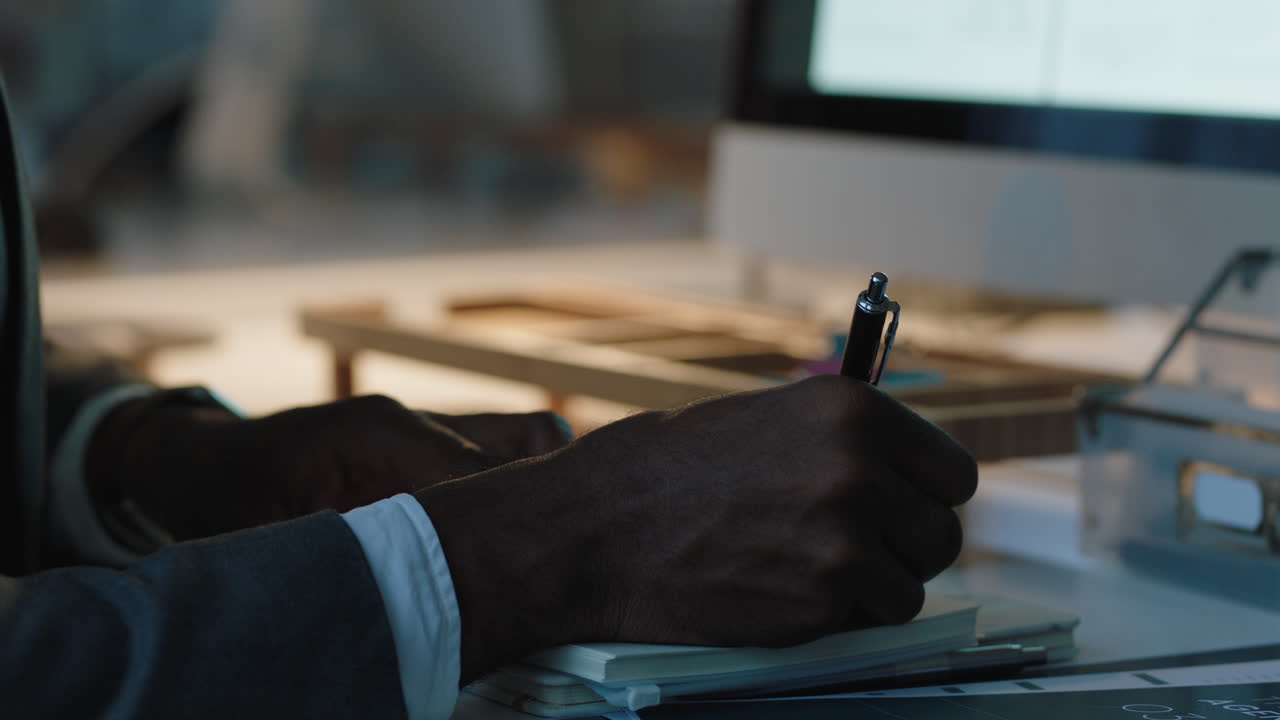 empresário afro-americano trabalhando até tarde usando computador escrevendo anotações brainstorming idéias planejamento de projetos prazo no espaço de trabalho do escritório