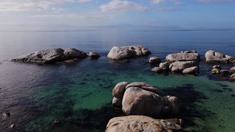 Drone-shot-flying-over-crystal-clear-ocean-water-with-birds-flying-around-over-large-rocks-in-the-seascape